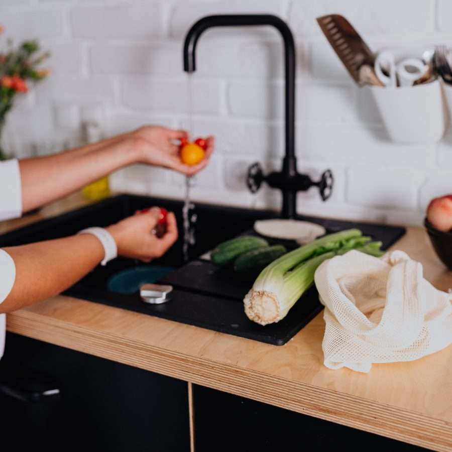 a woman washing fresh ingredients under a boiling water tap