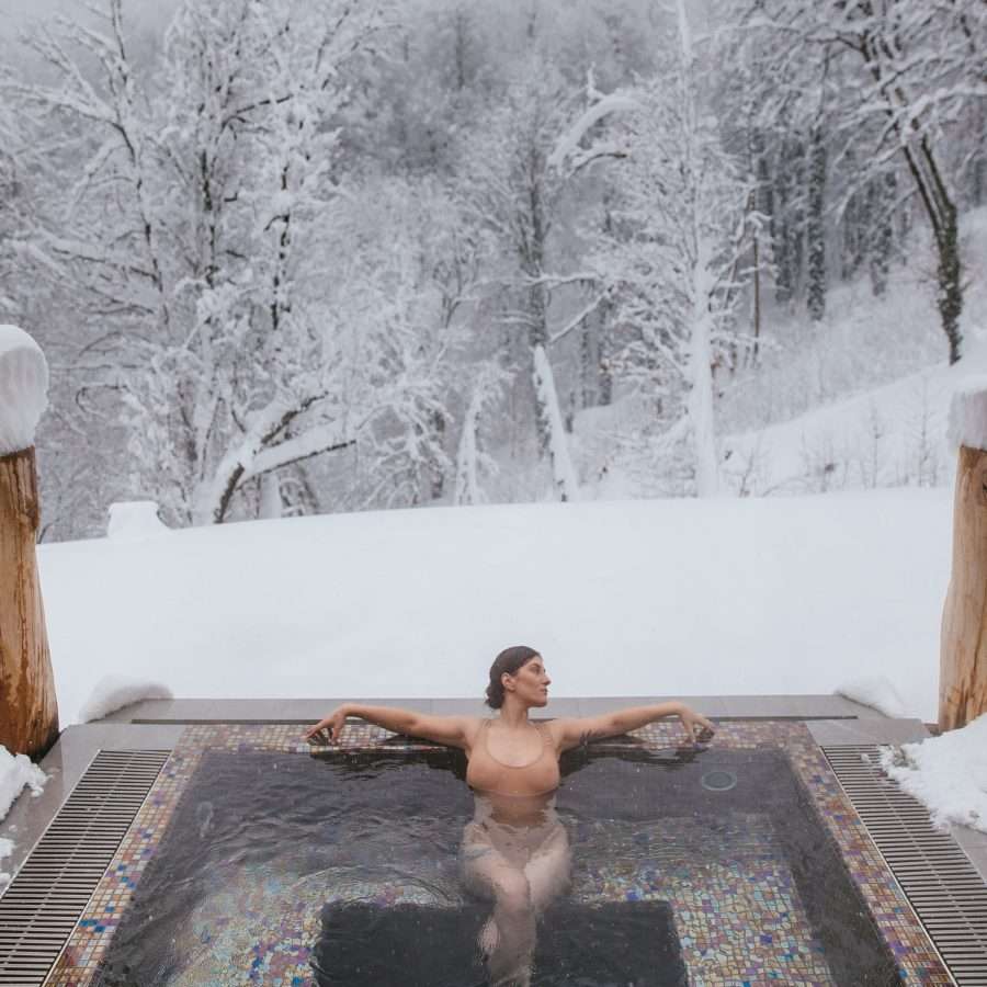 a woman in a hot tub near a snow-covered forest